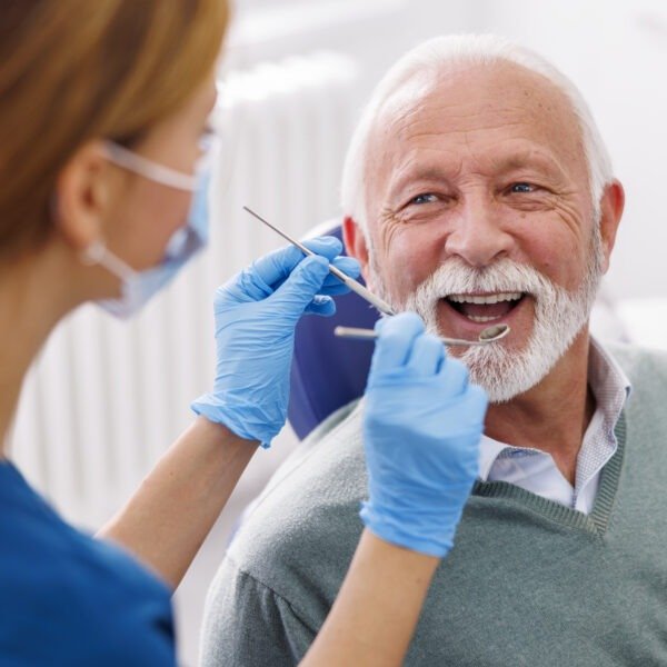 Doctor checking up patient's teeth at dentist office; senior man at dental checkup